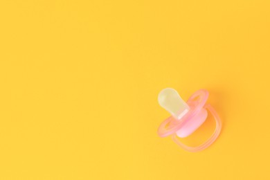 Photo of One new baby pacifier on orange background, top view. Space for text