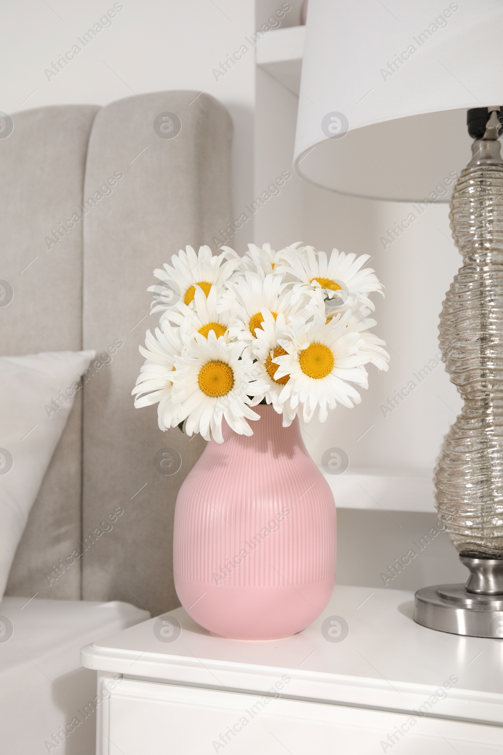 Bouquet of beautiful daisy flowers and lamp on nightstand in bedroom Photo of Bouquet of beautiful daisy flowers and lamp on nightstand in bedroom