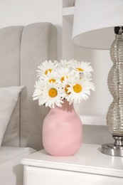 Photo of Bouquet of beautiful daisy flowers and lamp on nightstand in bedroom