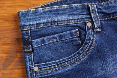Photo of Stylish blue jeans on wooden background, closeup of inset pocket