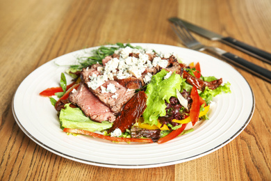 Photo of Delicious salad with roasted meat and vegetables served on wooden table