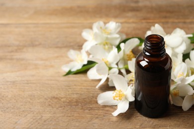 Photo of Jasmine essential oil and fresh flowers on wooden table, space for text
