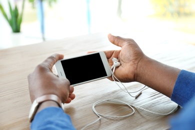 Photo of African-American man holding mobile phone with blank screen in hands at table indoors