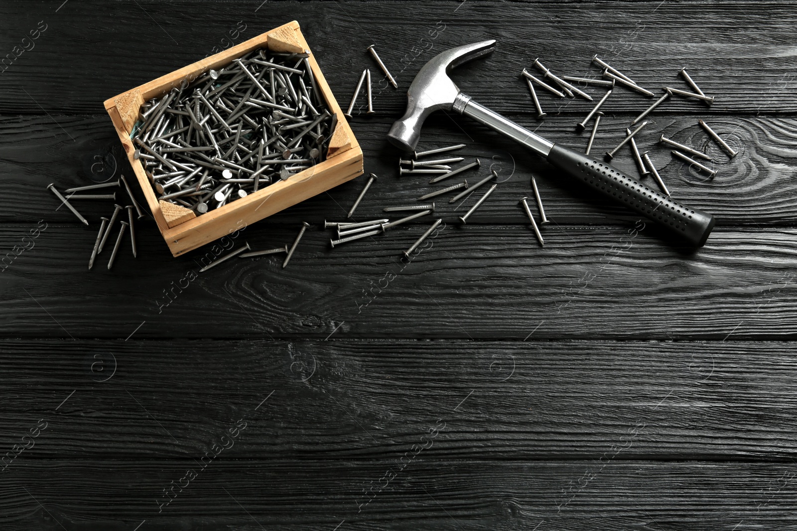 Photo of Hammer and metal nails on black wooden table, flat lay. Space for text