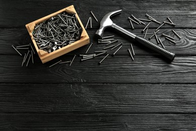 Photo of Hammer and metal nails on black wooden table, flat lay. Space for text