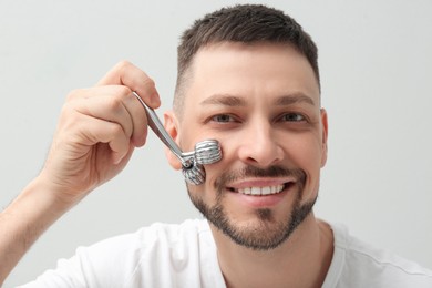 Photo of Man using metal facial roller on light background