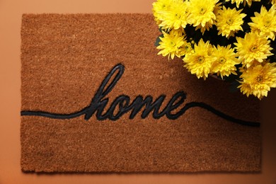 Photo of Doormat with word Home and flowers on brown background, flat lay