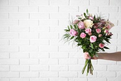 Photo of Woman with bouquet of beautiful roses near white brick wall, closeup. Space for text