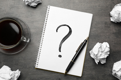 Image of Flat lay composition of crumpled paper balls and notebook with question mark on grey table