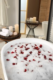 Photo of Bath tub with foam and red rose petals in bathroom