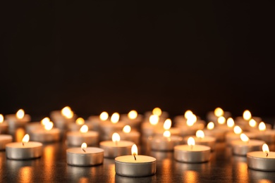 Photo of Many burning candles on table against dark background. Symbol of sorrow