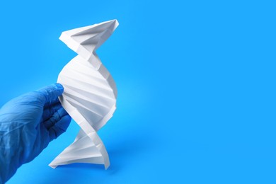 Photo of Scientist with DNA molecule model made of paper on light blue background, closeup. Space for text