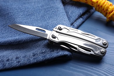 Photo of Modern compact portable multitool and jeans on blue wooden table
