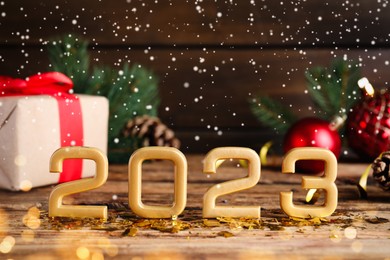Photo of Snow falling onto number 2023 and festive decor on wooden table, space for text. Happy New Year