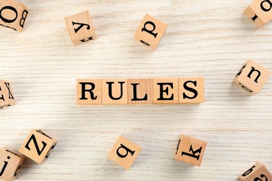 Photo of Word Rules made of cubes with letters on light wooden table, flat lay