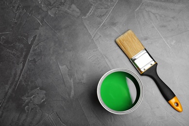 Photo of Can with green paint and brush on gray background, top view. Space for text