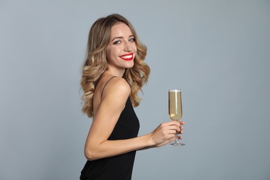 Photo of Happy young woman with glass of champagne on grey background. Christmas celebration