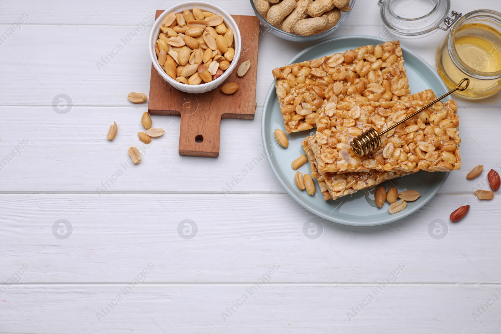 Photo of Delicious peanut bars (kozinaki) and ingredients on white wooden table, flat lay. Space for text