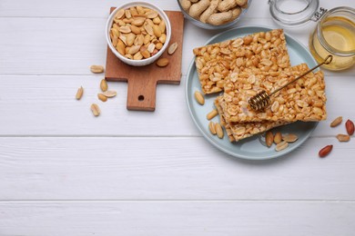 Photo of Delicious peanut bars (kozinaki) and ingredients on white wooden table, flat lay. Space for text