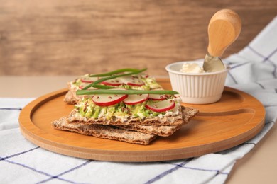 Photo of Fresh crunchy crispbreads with cream cheese, radish and green onion on beige table