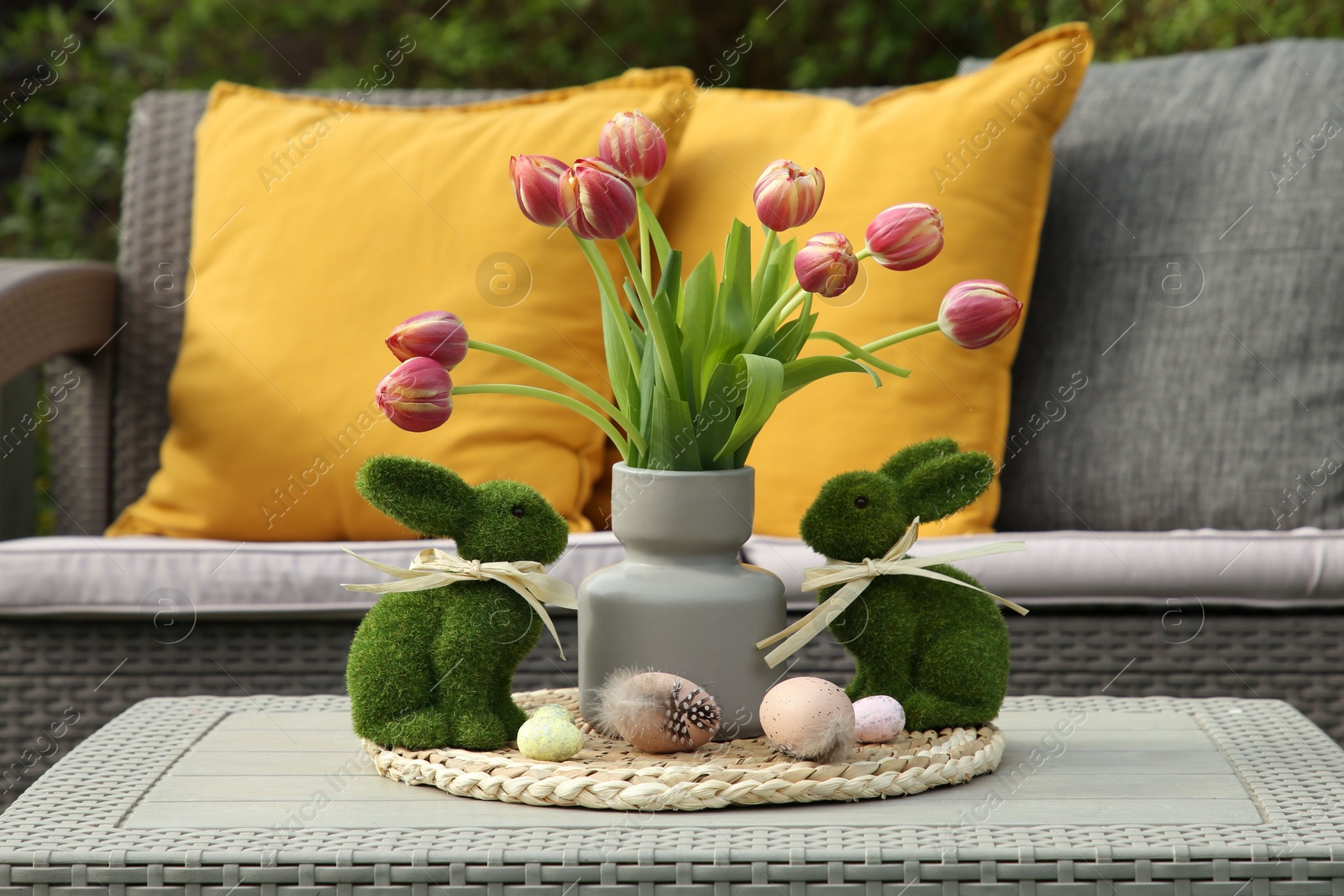 Photo of Terrace with Easter decorations. Bouquet of tulips in vase, bunny figures and decorated eggs on table outdoors