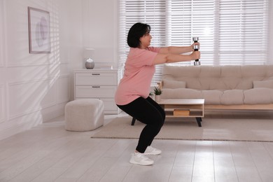 Photo of Overweight mature woman doing exercise with dumbbells at home
