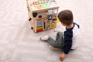 Little boy playing with busy board house on floor indoors