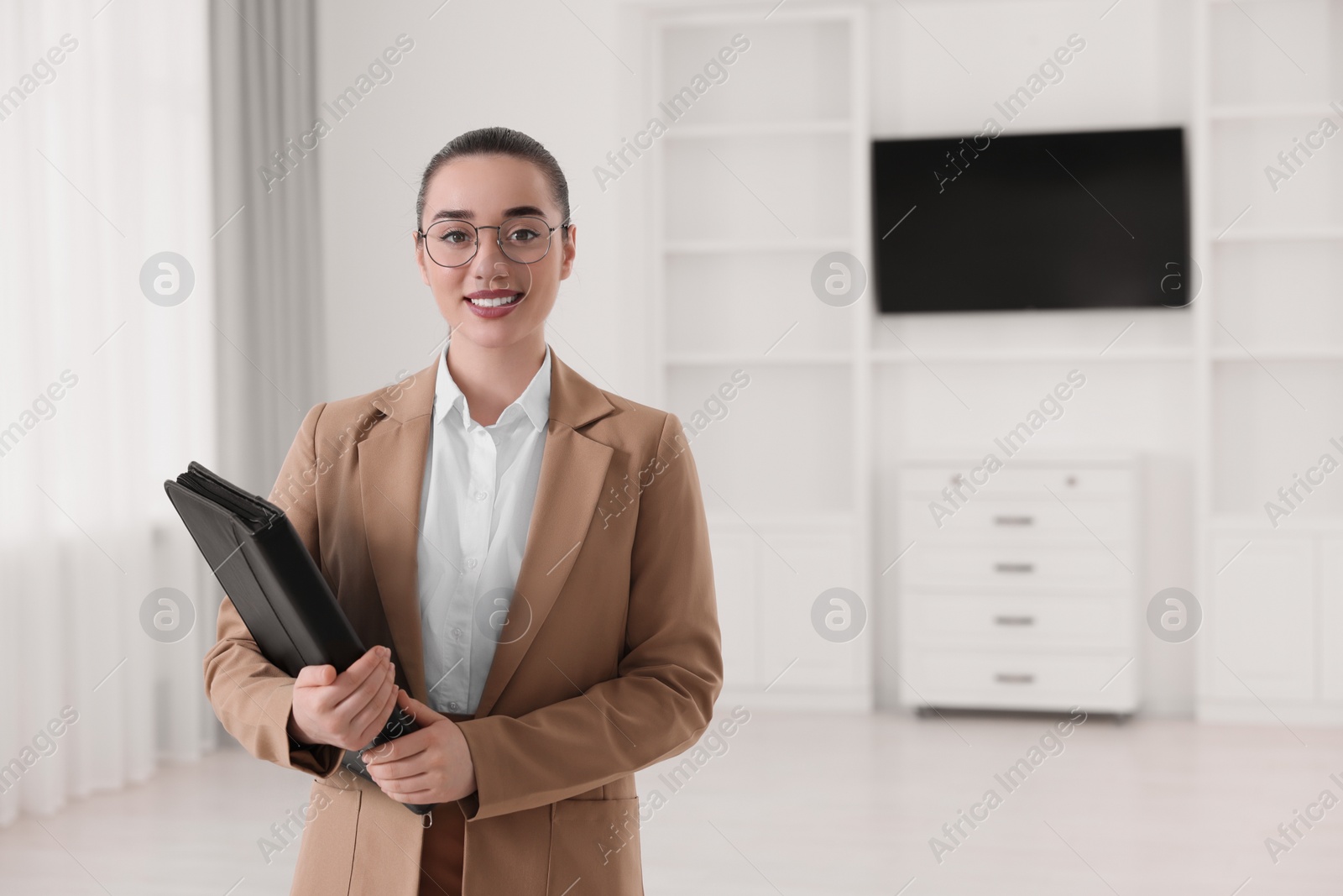 Photo of Happy real estate agent with leather portfolio indoors. Space for text