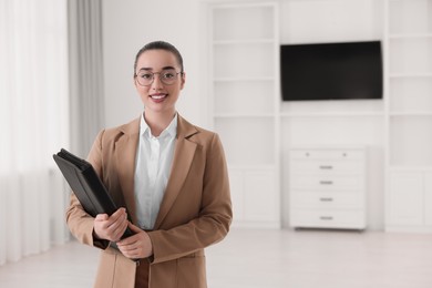 Photo of Happy real estate agent with leather portfolio indoors. Space for text