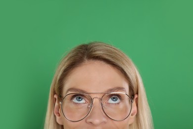 Photo of Woman in glasses looking up on green background, closeup