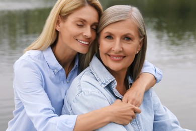 Photo of Happy mature mother and her daughter hugging near pond