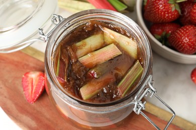 Photo of Jar of tasty rhubarb jam and strawberries on table, above view