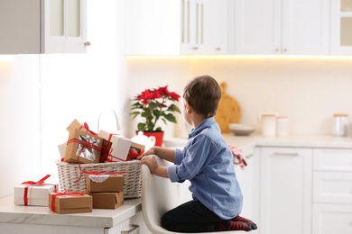 Photo of Little boy with Christmas gifts at home. Advent calendar in basket