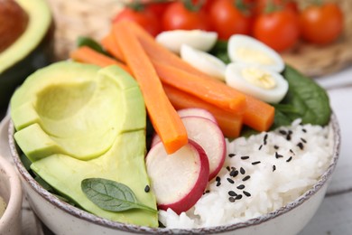 Delicious poke bowl with basil, eggs, avocado and vegetables on white wooden table, closeup