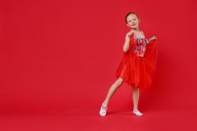 Photo of Cute little girl dancing on red background, space for text