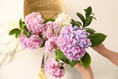 Photo of Woman making bouquet with beautiful hydrangea flowers indoors, top view. Interior design element
