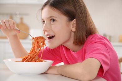 Photo of Happy girl eating tasty pasta at table in kitchen