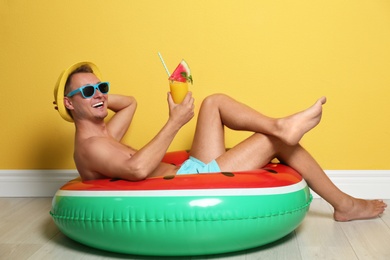 Photo of Shirtless man with inflatable ring and glass of cocktail on floor near color wall