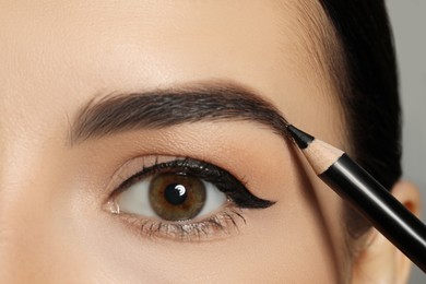 Young woman correcting eyebrow shape with pencil, closeup view