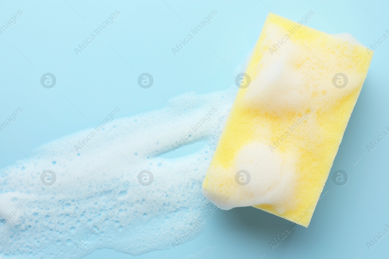 Yellow sponge with foam on light blue background, top view Photo of Yellow sponge with foam on light blue background, top view