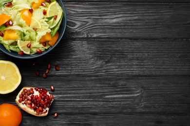 Photo of Delicious salad with Chinese cabbage, lemon, persimmon and pomegranate seeds on black wooden table, flat lay. Space for text