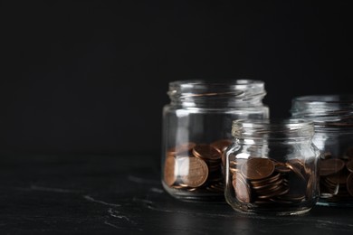 Photo of Glass jars with coins on black marble table, closeup. Space for text