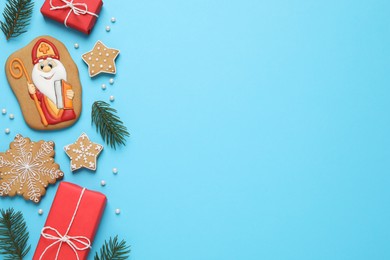 Photo of Tasty gingerbread cookies and fir branches on light blue background, flat lay with space for text. St. Nicholas Day celebration
