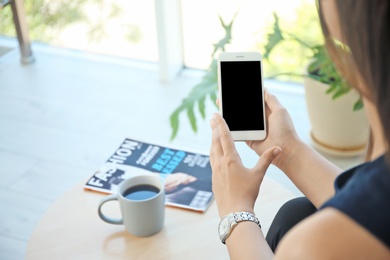 Photo of Young woman holding mobile phone with blank screen in hands indoors