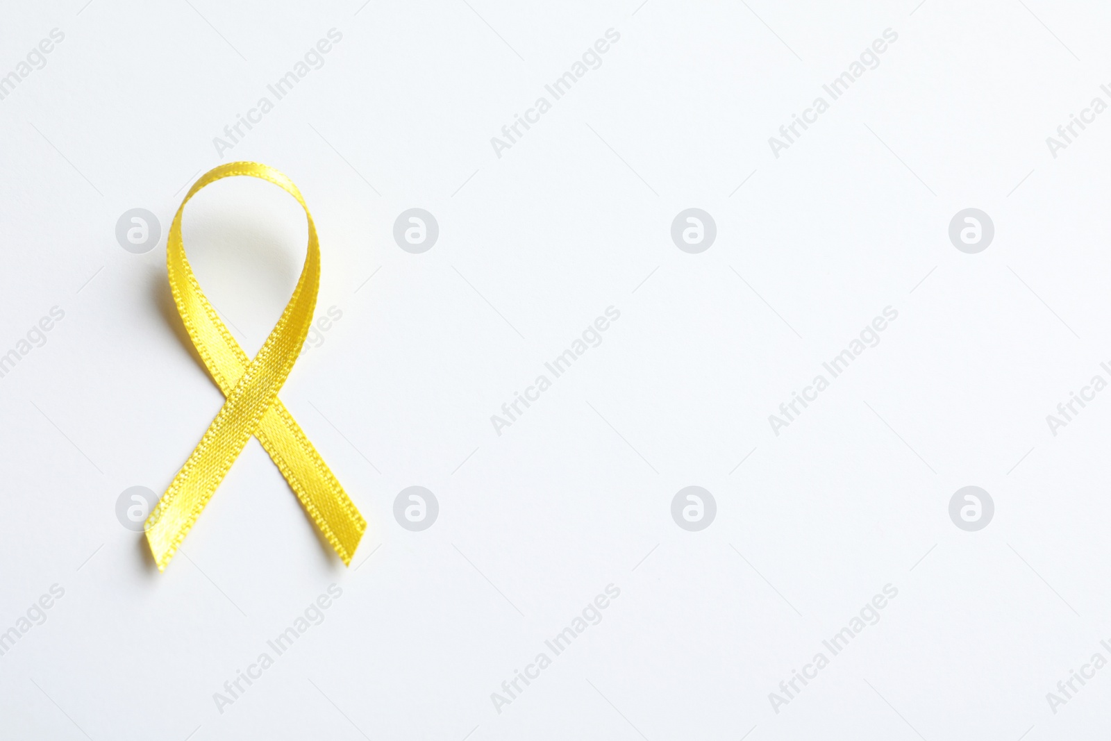 Photo of Yellow ribbon on white background, top view. Cancer awareness