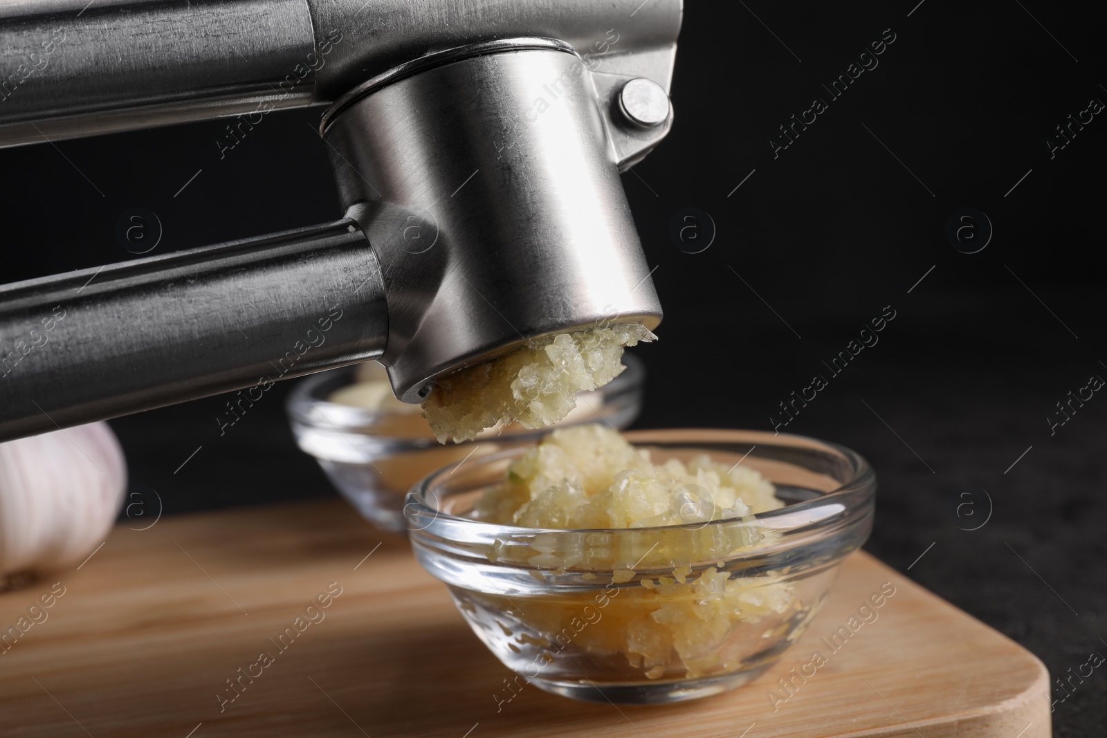 Photo of Crushing garlic with press into bowl at wooden table, closeup