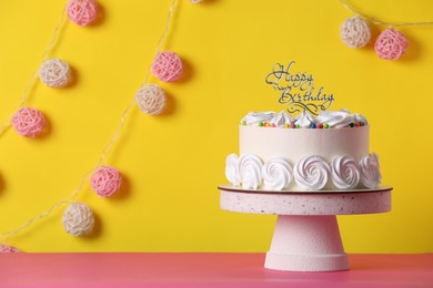 Photo of Beautifully decorated birthday cake on pink table near yellow wall, space for text