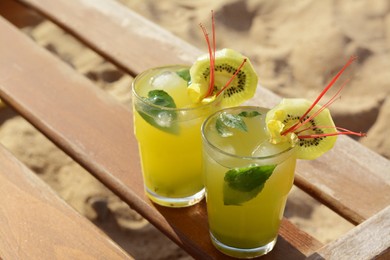 Photo of Glasses of refreshing drink with kiwi and mint on wooden bench at beach