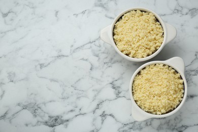 Photo of Bowls with tasty couscous on white marble table, flat lay. Space for text