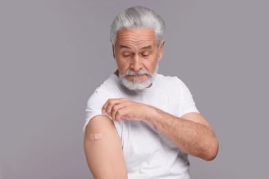 Photo of Senior man with adhesive bandage on his arm after vaccination against light grey background